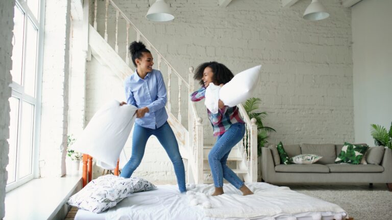 Two women having a pillow fight on a bed.