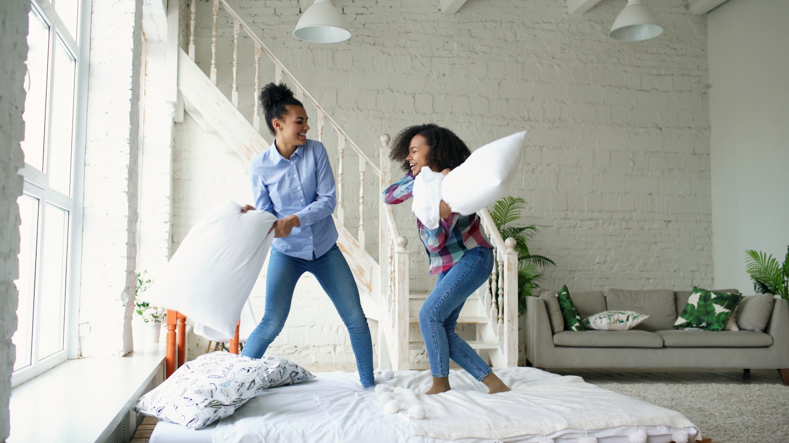 Two women having a pillow fight on a bed.