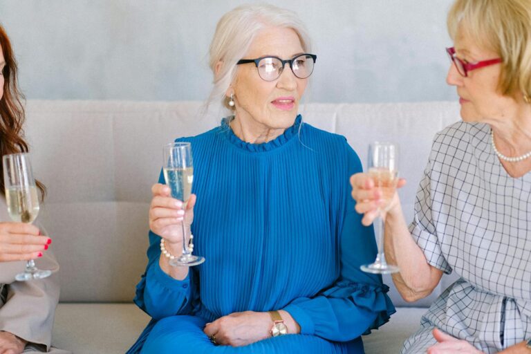 Three elegantly dressed senior women enjoying a champagne toast at a social gathering.