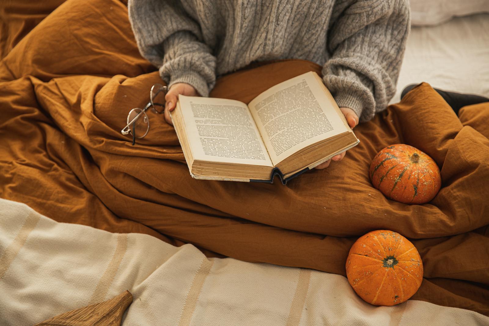 A person reading a book in a cozy setting with pumpkins, embodying autumn relaxation.