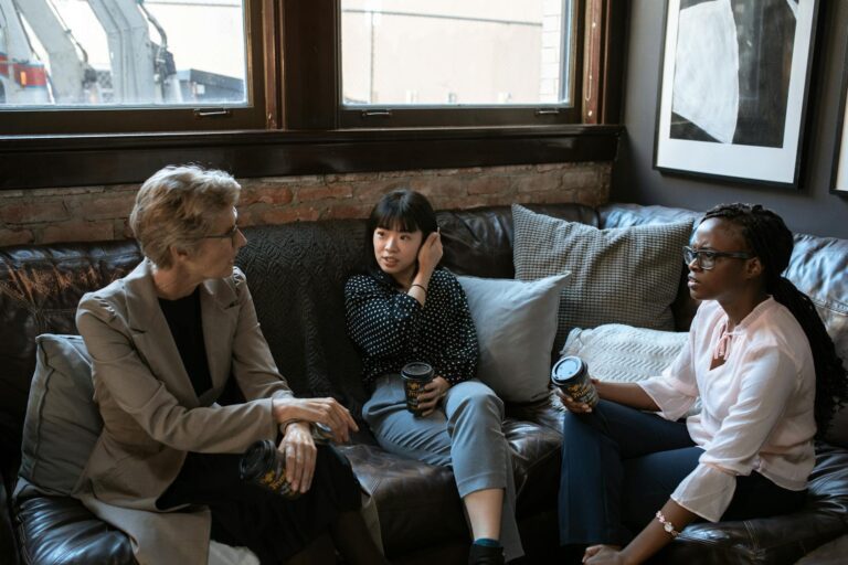 Three diverse women enjoying a coffee break and engaging in conversation in a stylish office setting.
