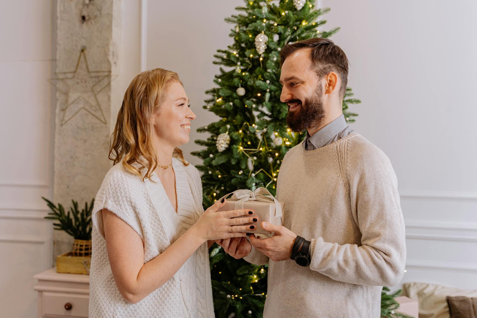 A smiling couple exchanges a gift in front of a decorated Christmas tree, adding warmth and joy to the holiday season.