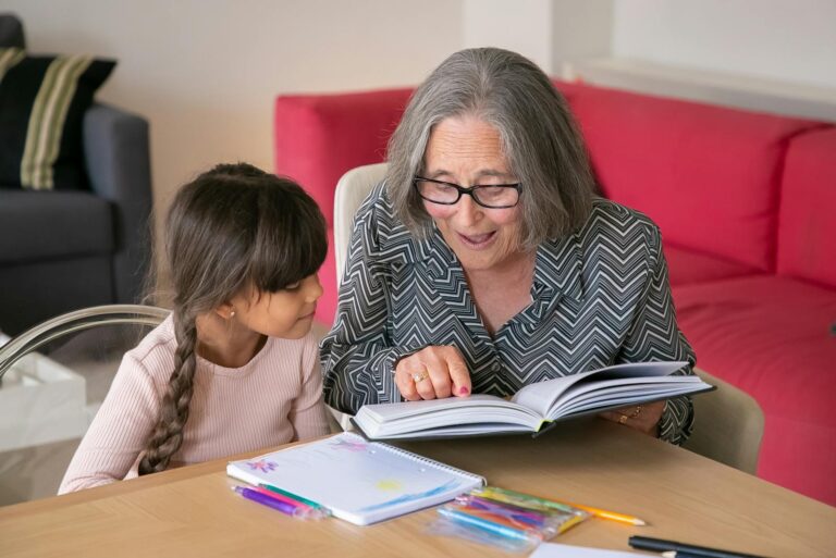 A joyful grandmother reading a book with her granddaughter indoors, bonding over learning.