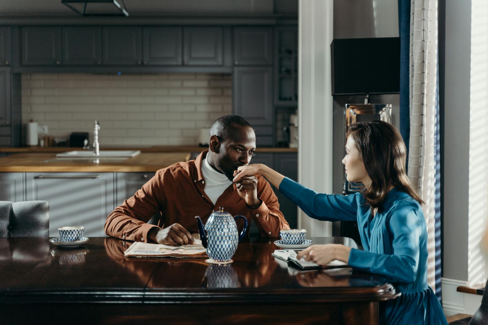 A romantic couple sharing a moment over tea at a wooden table in a cozy kitchen.