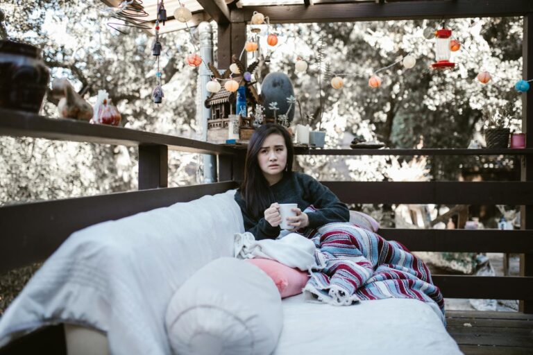 Woman enjoying a quiet afternoon with tea on a patio, wrapped in a colorful blanket.