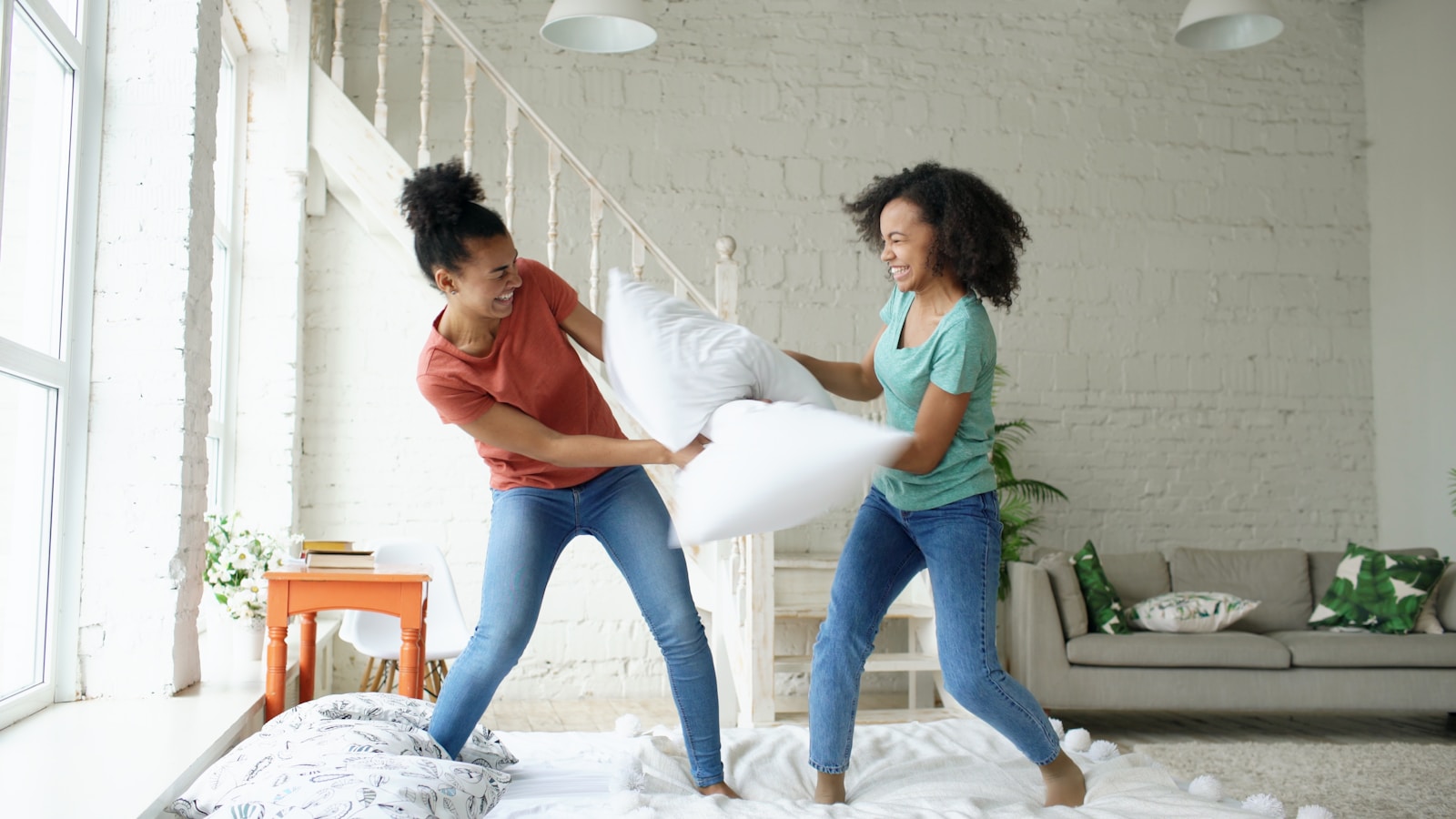 Two young women having a pillow fight indoors.