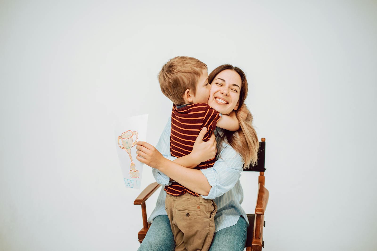 A joyful child hugging his smiling mother while holding a trophy drawing.