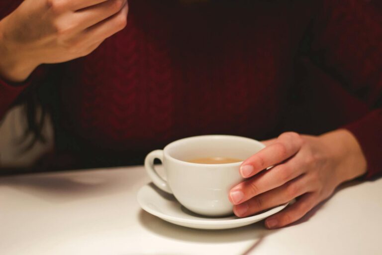 Close-up of a person holding a cup of coffee indoors, creating a cozy and warm atmosphere.