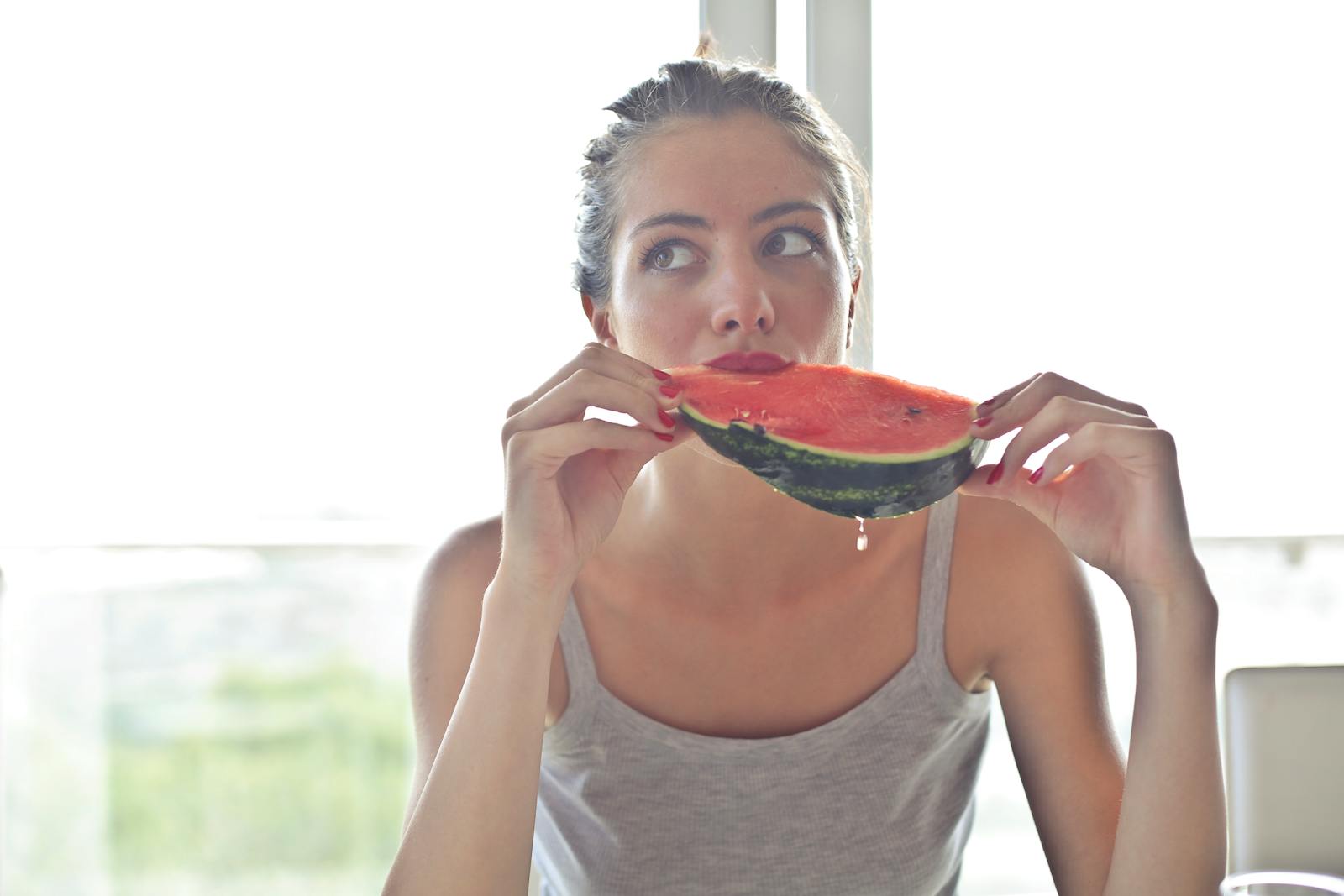 Portrait of a woman eating watermelon indoors, reflecting health and summer vibes.