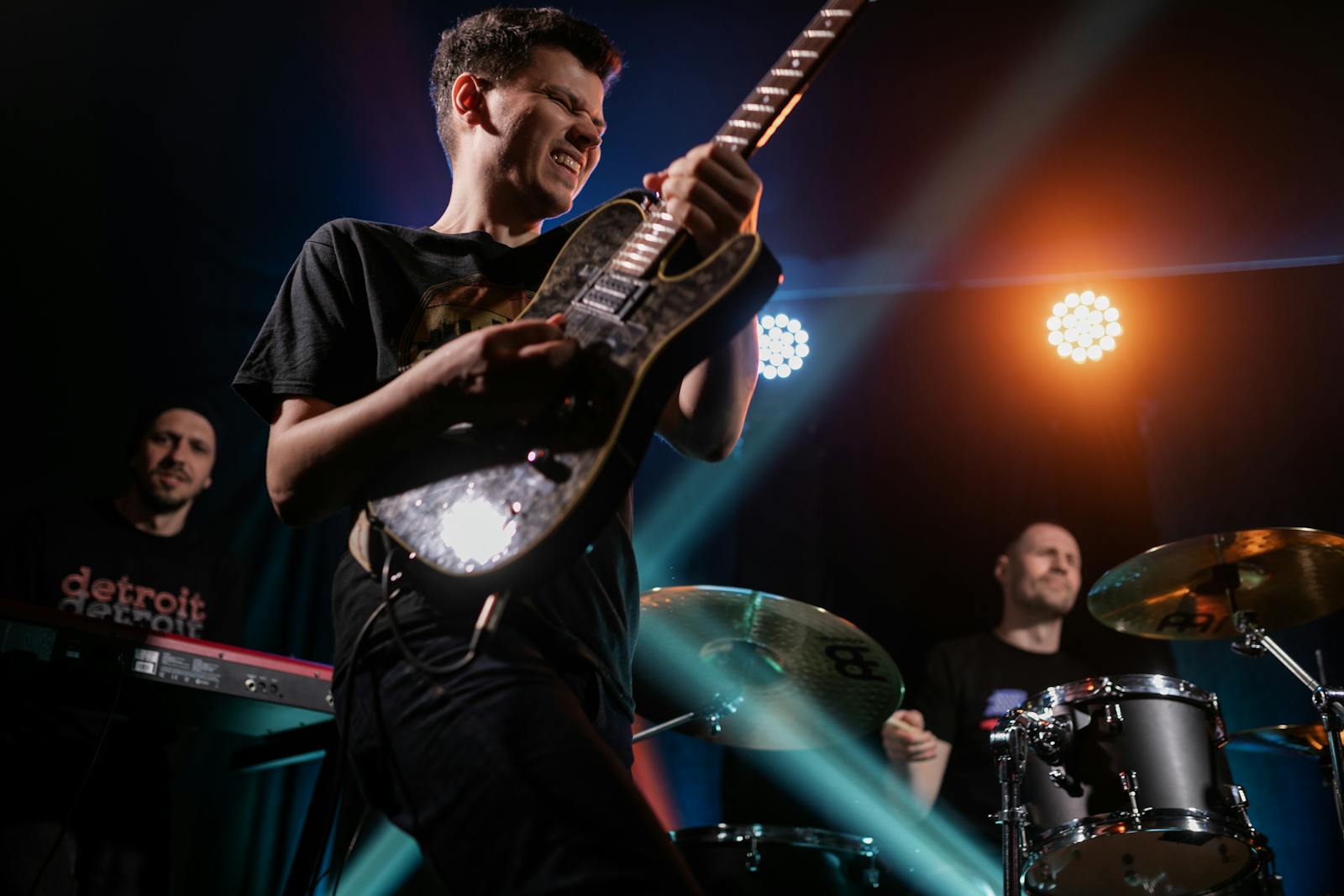 Vibrant live rock band performing on stage with guitarist, drummer, and keyboardist.