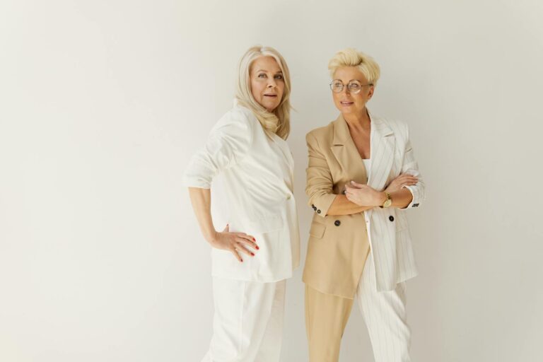 Two confident businesswomen in fashionable suits pose against a white background.
