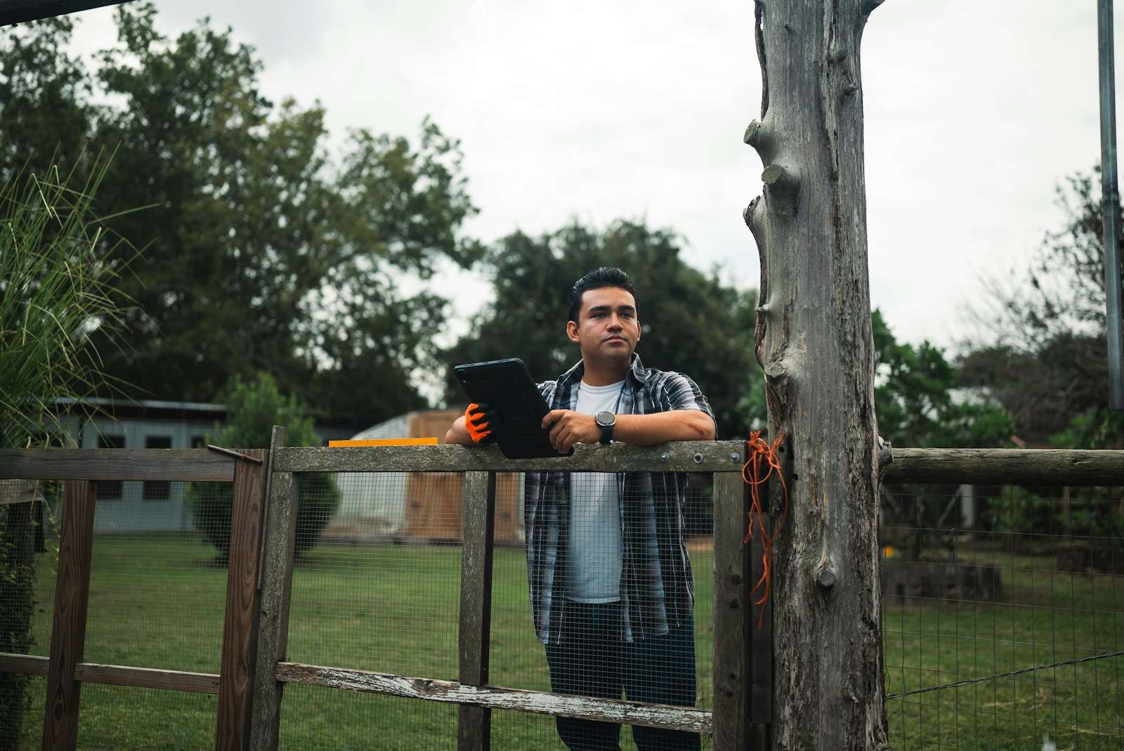Man holding tablet standing by a wooden fence outdoors