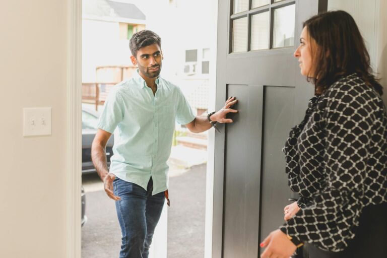 A man enters a home, conversing with a woman standing nearby in a casual setting.