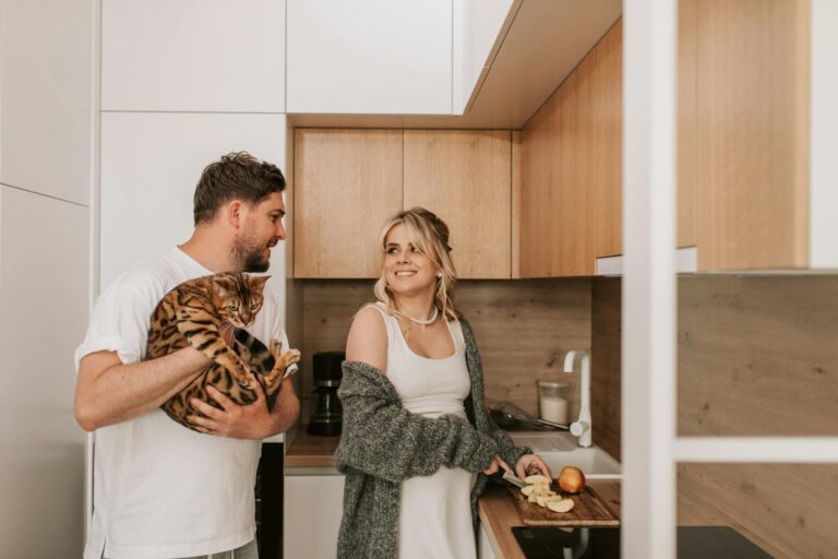 A couple enjoys a cozy moment in their modern kitchen with a Bengal cat, cooking and sharing smiles.