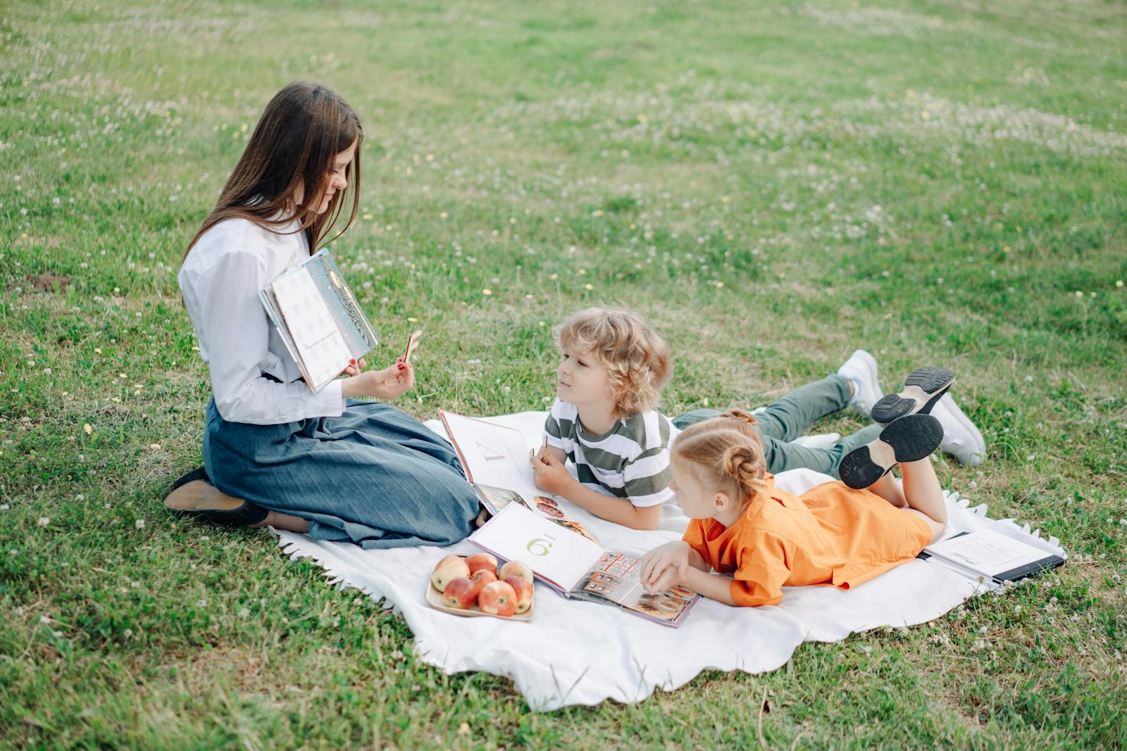 A young teacher conducting an outdoor learning session with children, engaging in interactive study on a grassy field.