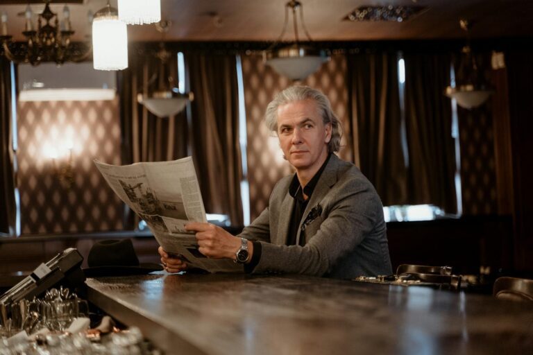 Mature man in a stylish suit reads a newspaper at an elegant bar, exuding sophistication and class.