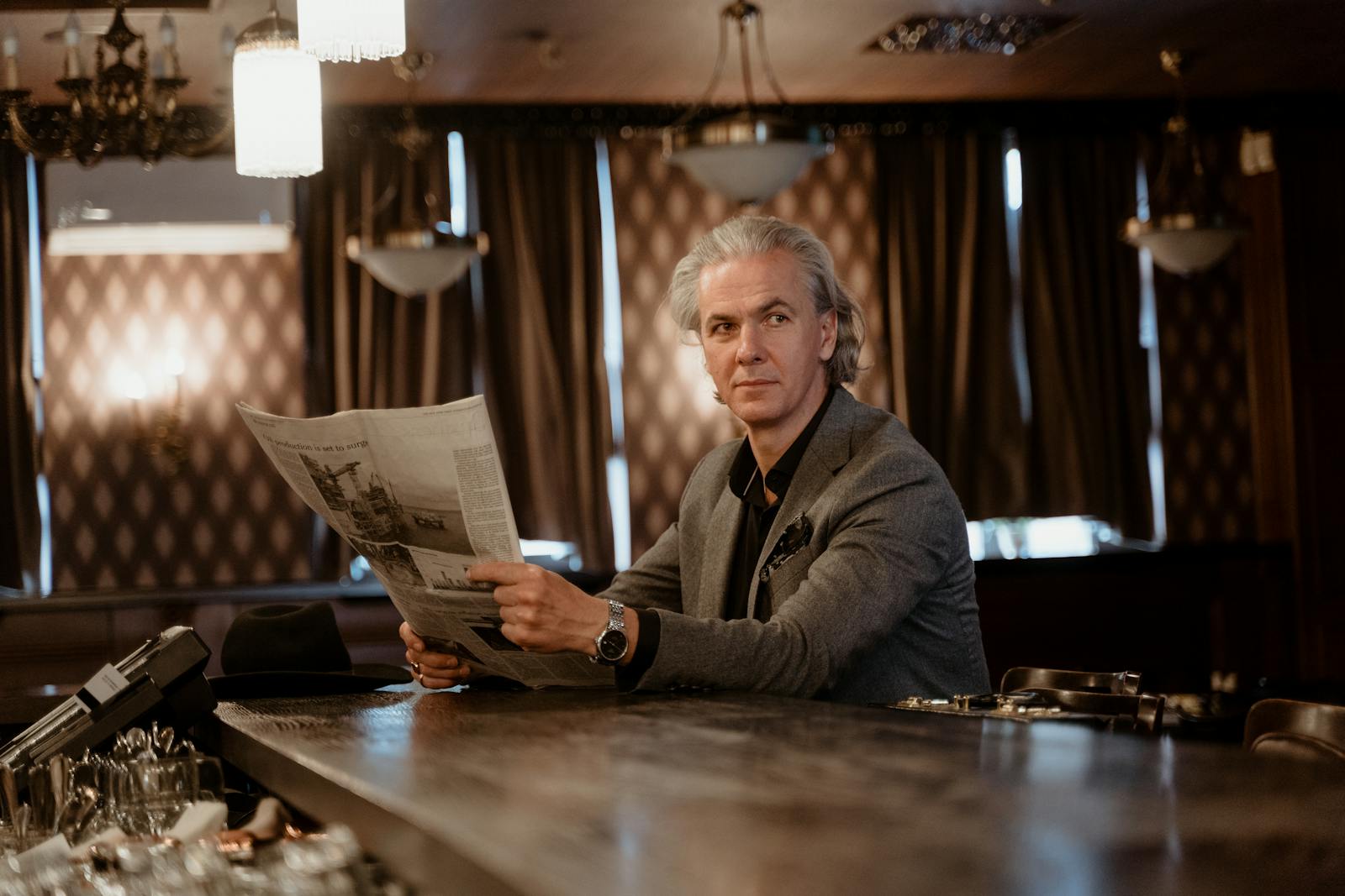 Mature man in a stylish suit reads a newspaper at an elegant bar, exuding sophistication and class.