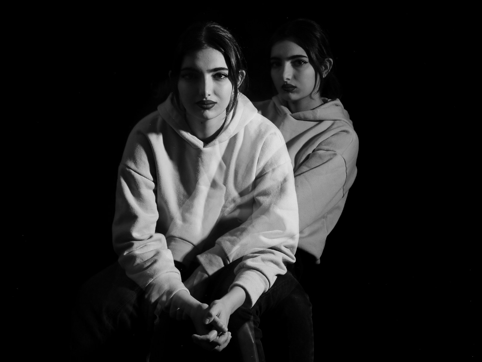 Two young women in hoodies against a dark background