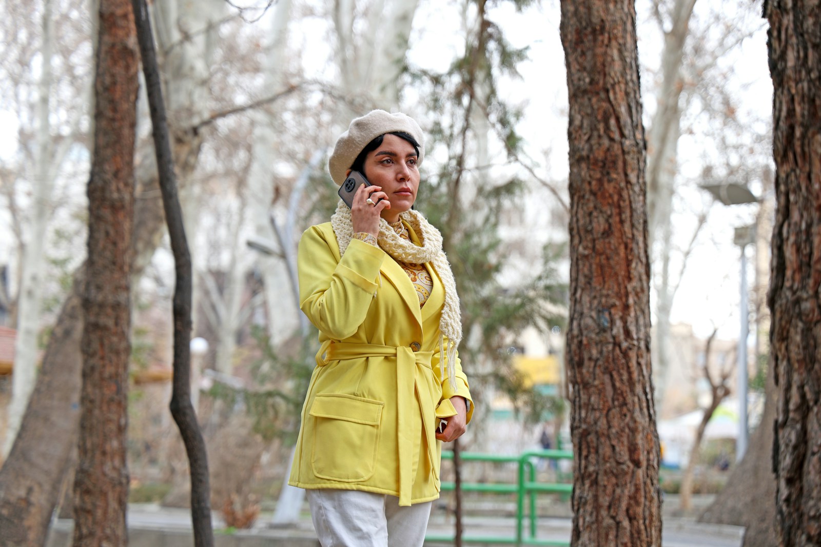 Woman in yellow coat talking on phone in park