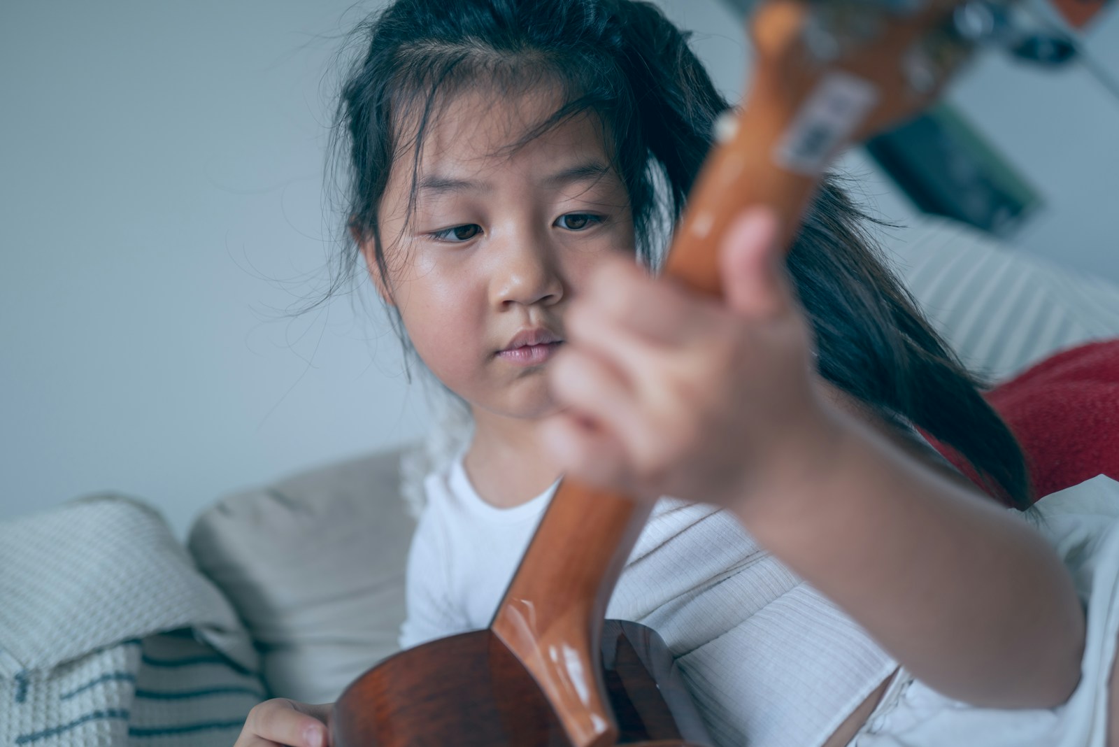 Young girl plays the ukulele intently.