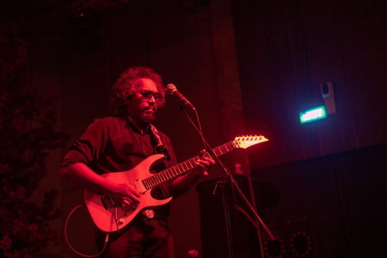 Man playing electric guitar on stage with red lighting