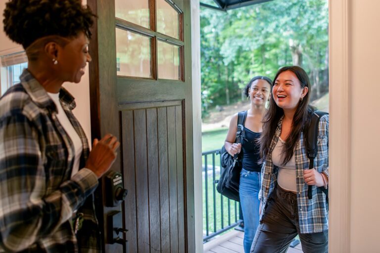 Two women arriving at a doorway, greeted by another woman.