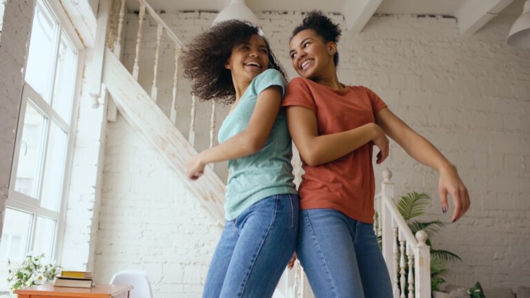 Two smiling women dancing back to back indoors