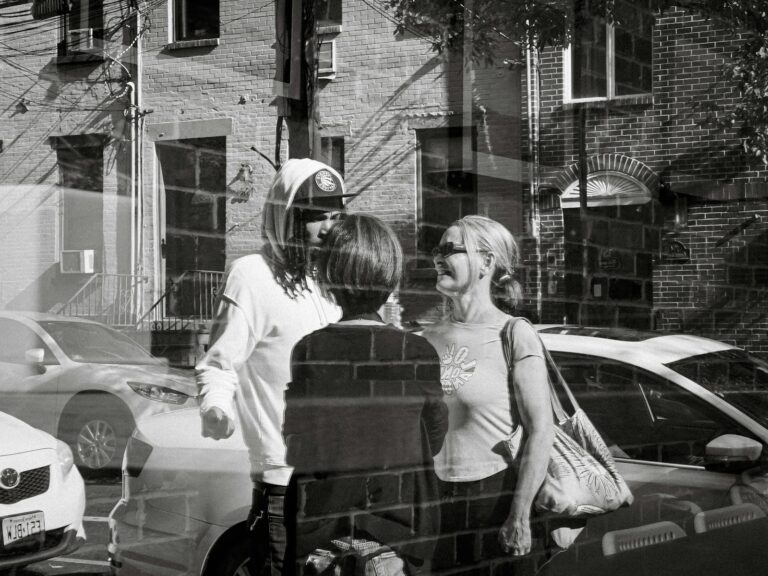Three people talk on a street with cars.