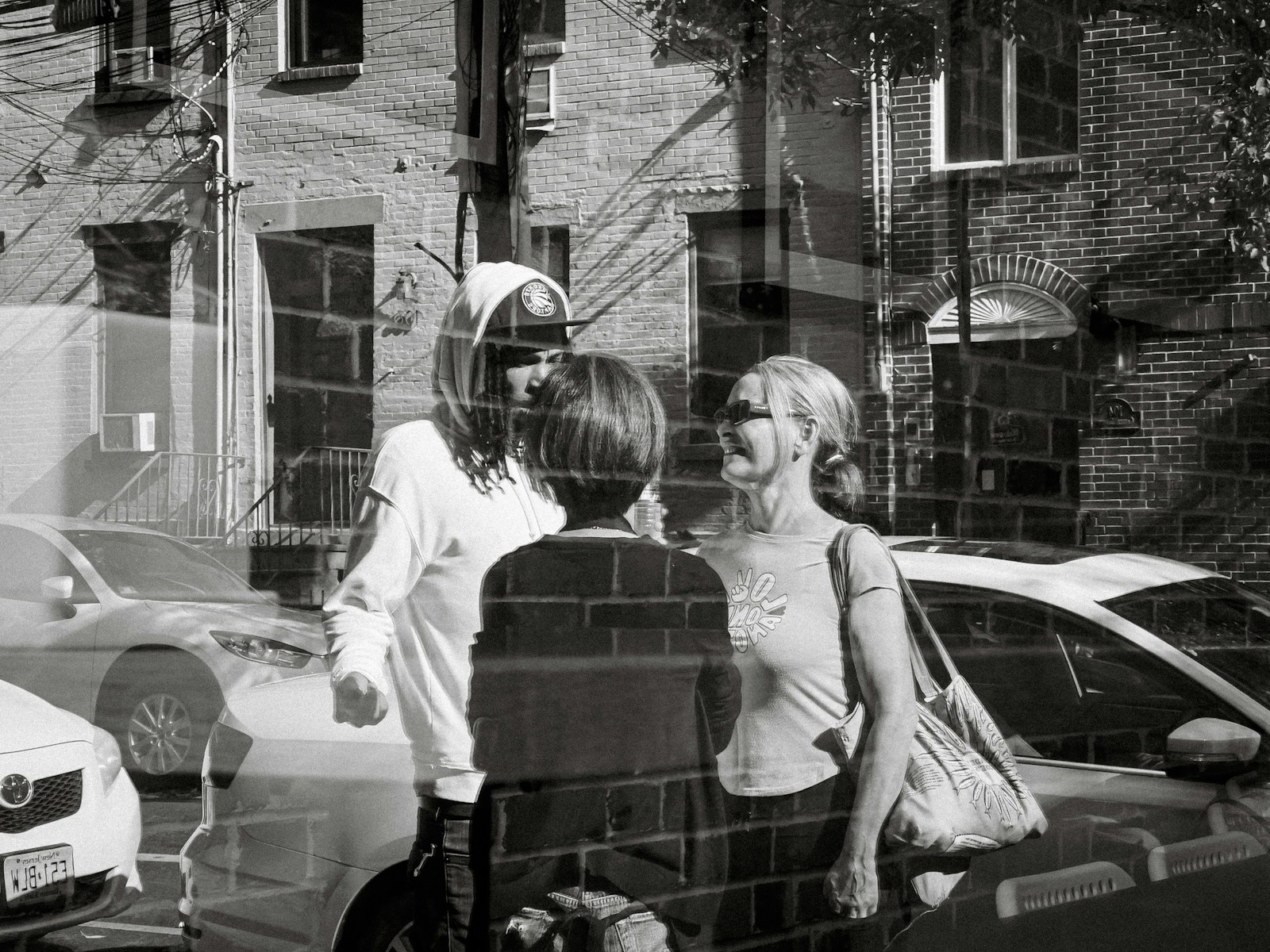 Three people talk on a street with cars.