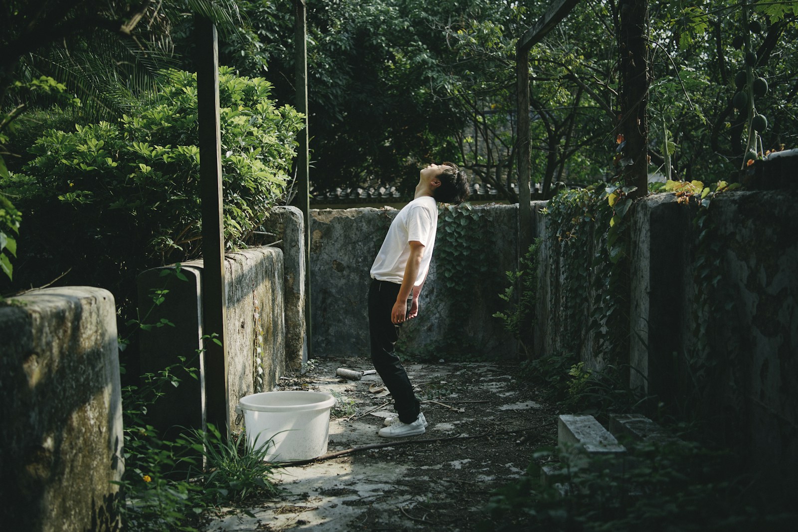 man in white t-shirt and black pants standing on gray concrete pathway