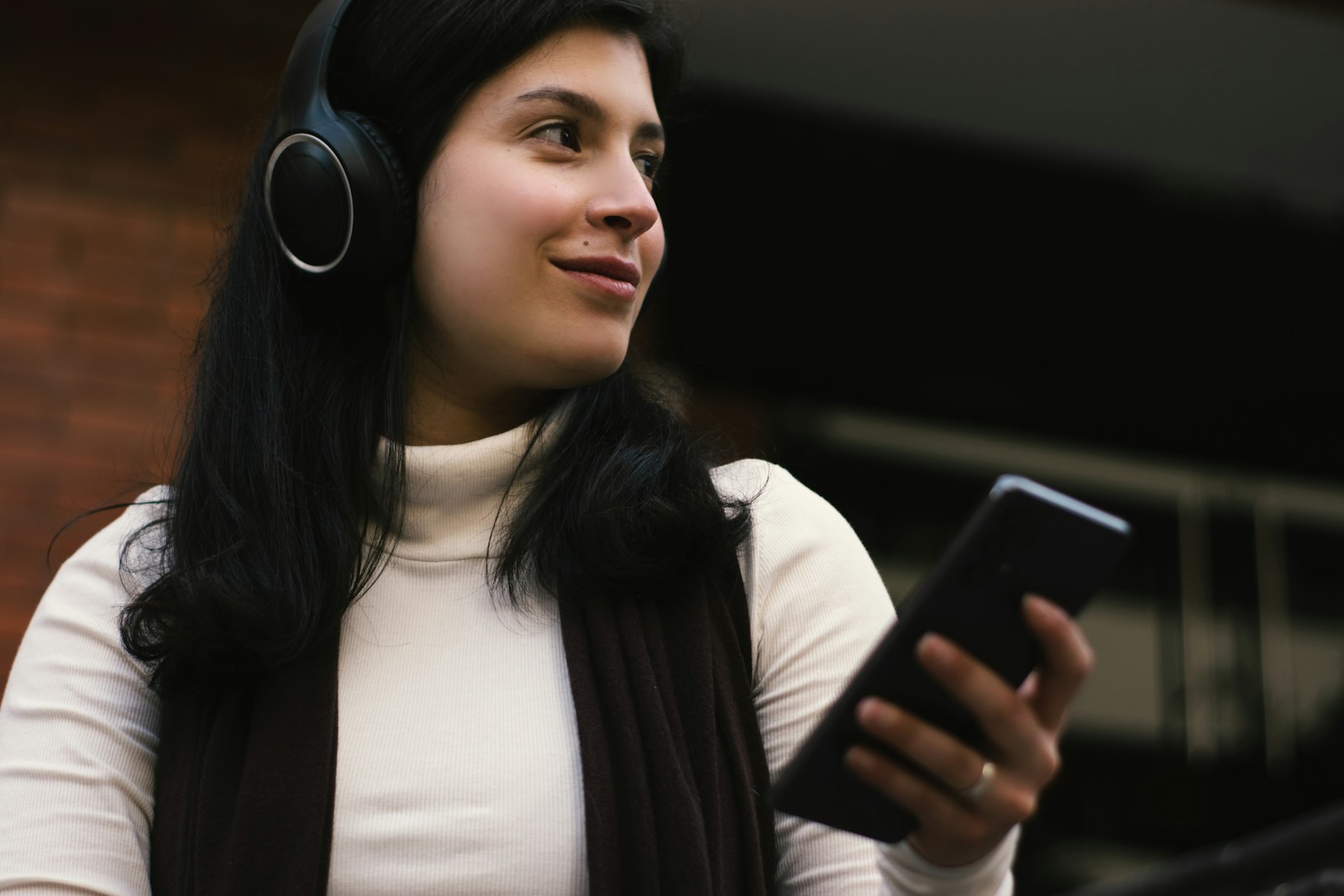 Woman wearing headphones holds a smartphone