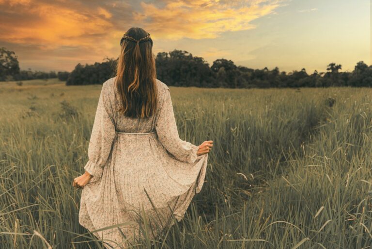 woman in white long sleeve dress standing on green grass field during sunset