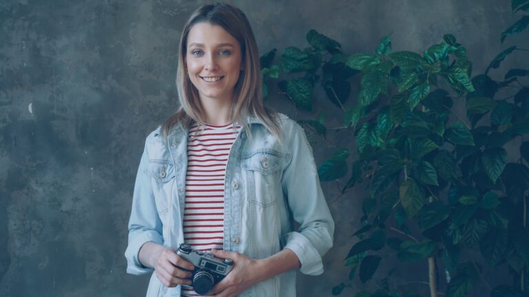 Woman smiles while holding a camera.