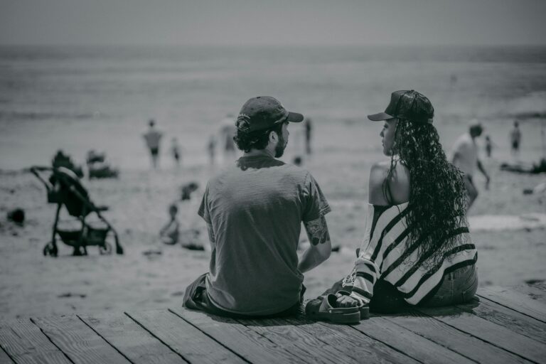 a man and a woman sitting on a pier looking at the beach