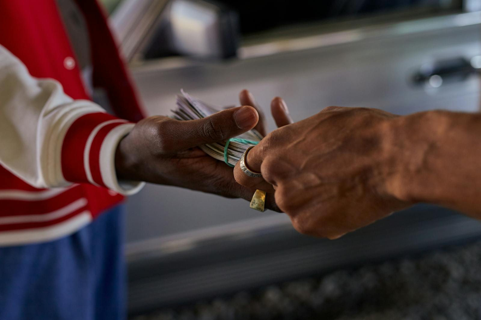 A detailed shot of two hands exchanging a bundle of cash outside by a car.