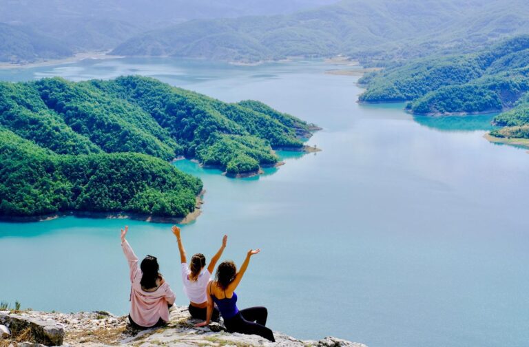 Three friends enjoying the stunning view of Lake Bovilla, Albania from a cliff.