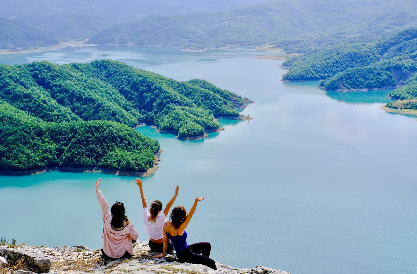 Three friends enjoying the stunning view of Lake Bovilla, Albania from a cliff.