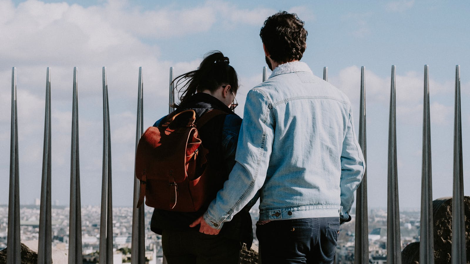 A couple stands on an observation deck overlooking a cityscape, enjoying a bright day together.