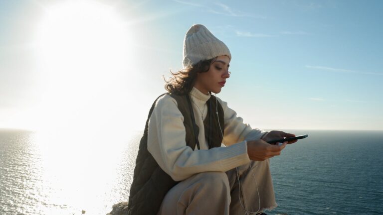 Serene moment of a woman enjoying music by the sea at sunset in Sesimbra, Portugal.