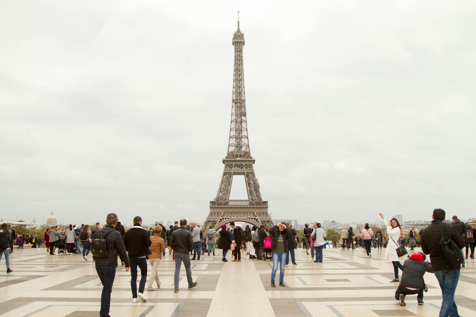 Crowd of tourists at the iconic Eiffel Tower in Paris on an overcast day.