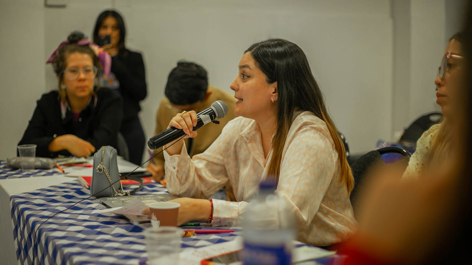 Woman participating in a group discussion, holding a microphone at a table indoors.