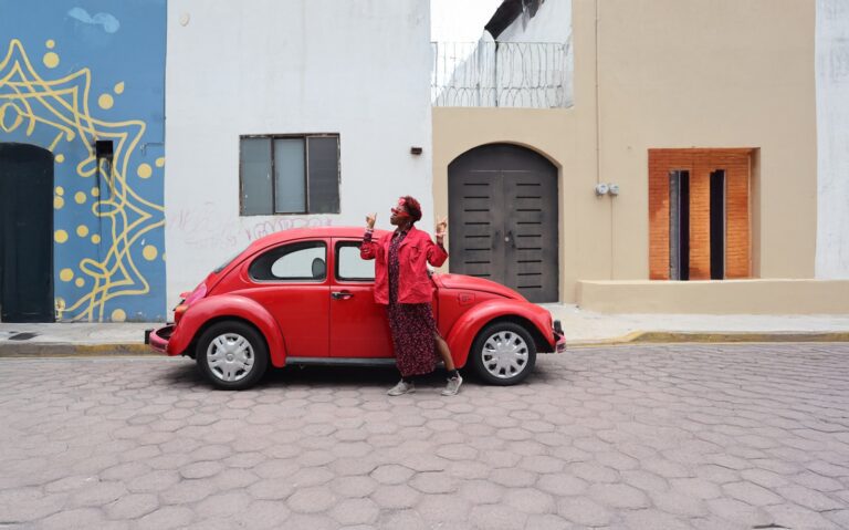 A person poses with a red volkswagen beetle.