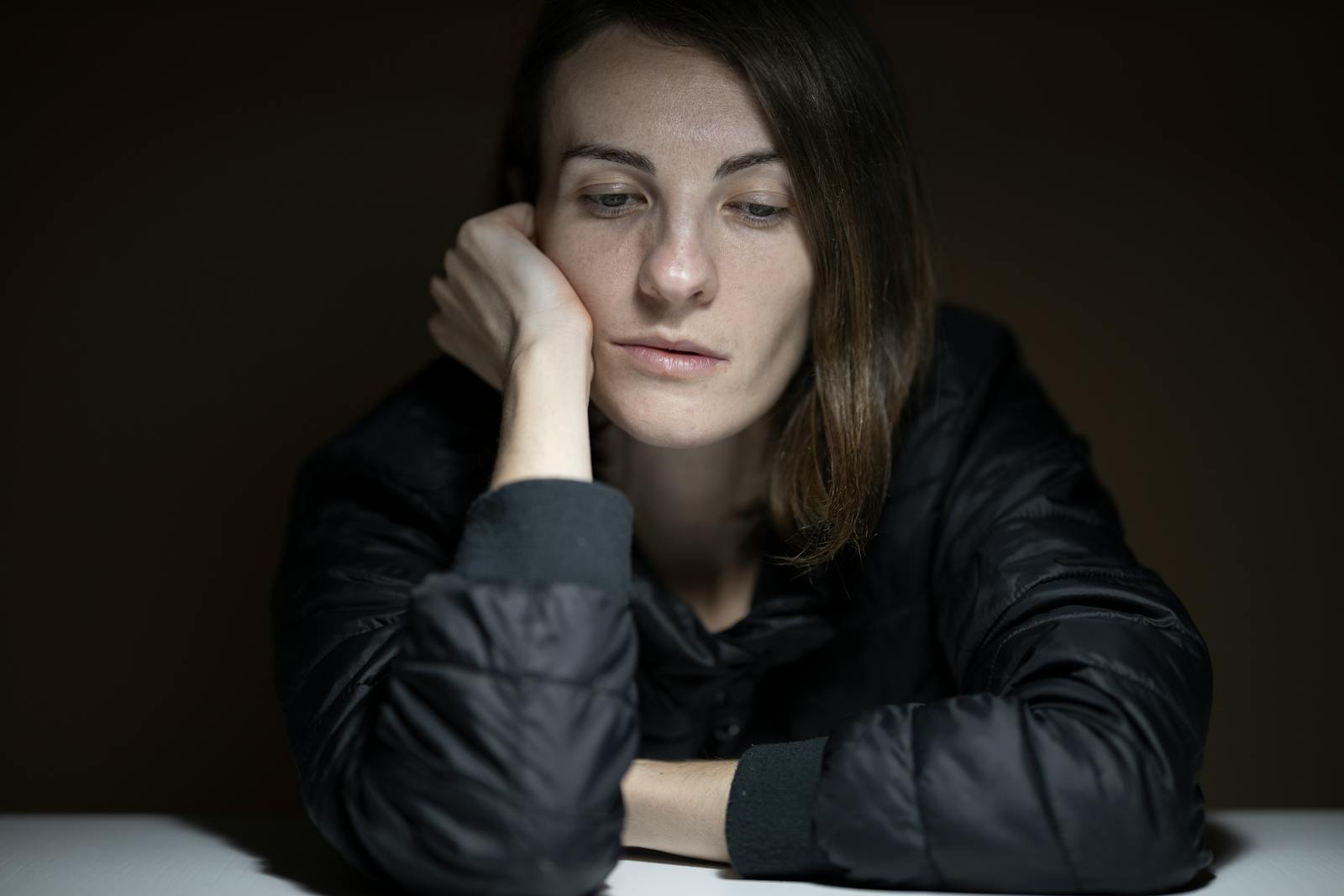 A woman in thought with a serious expression, indoors, in a low-light setting.