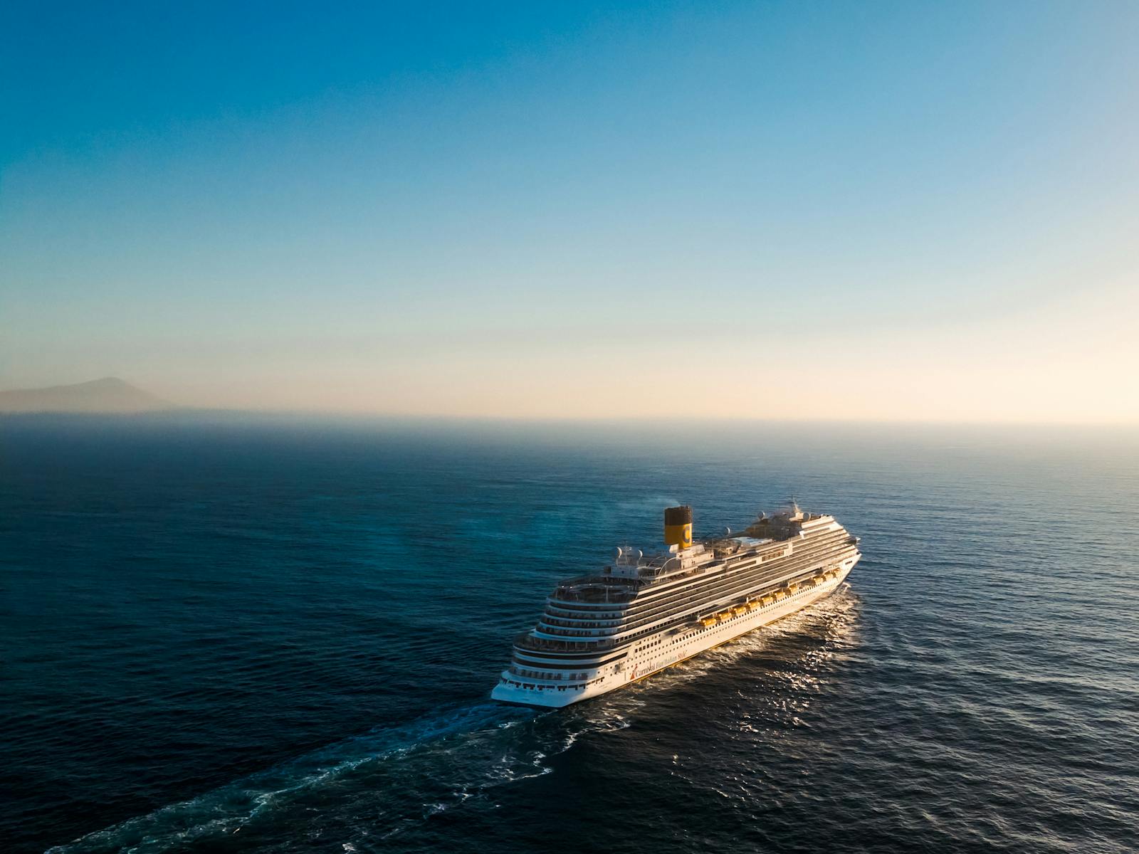 Aerial view of a luxury cruise ship navigating the calm ocean waters during sunset.