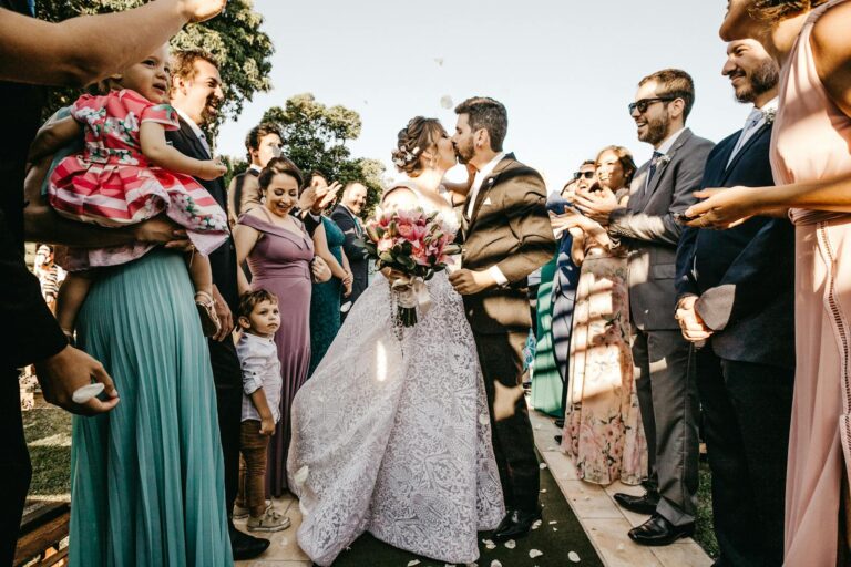 Outdoor wedding ceremony capturing a newlywed kiss as guests celebrate on a sunny day.