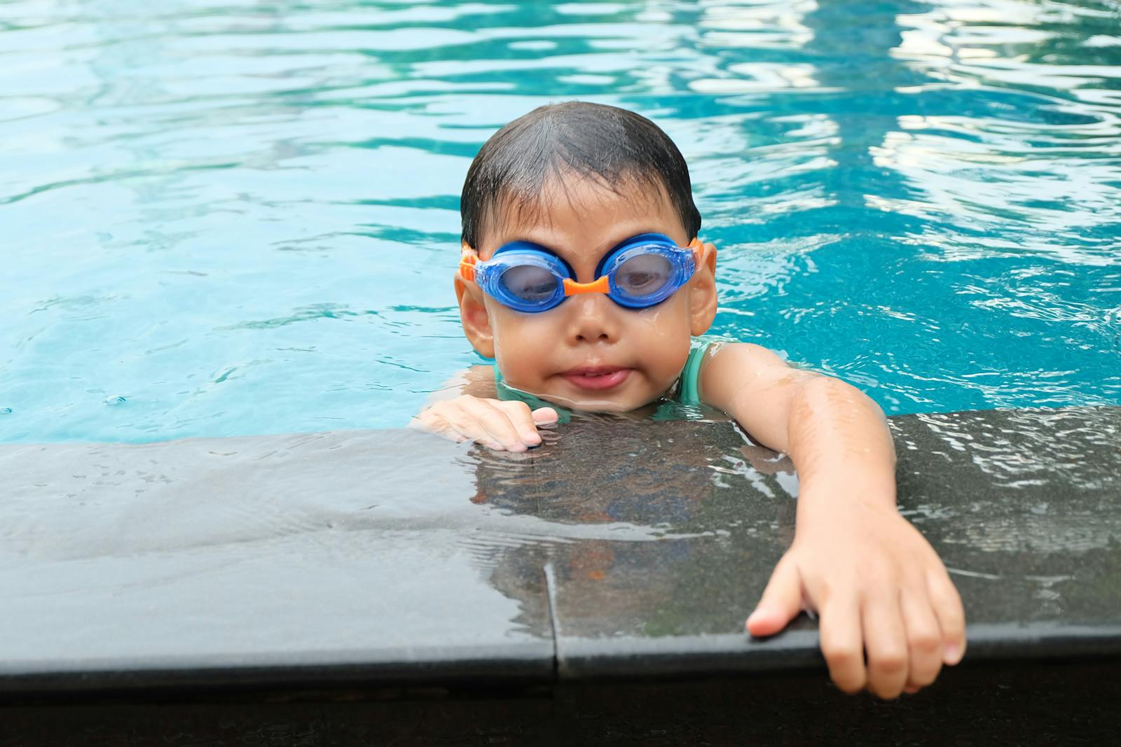 Young child enjoys swimming in a pool wearing blue goggles, showcasing aquatic activities.