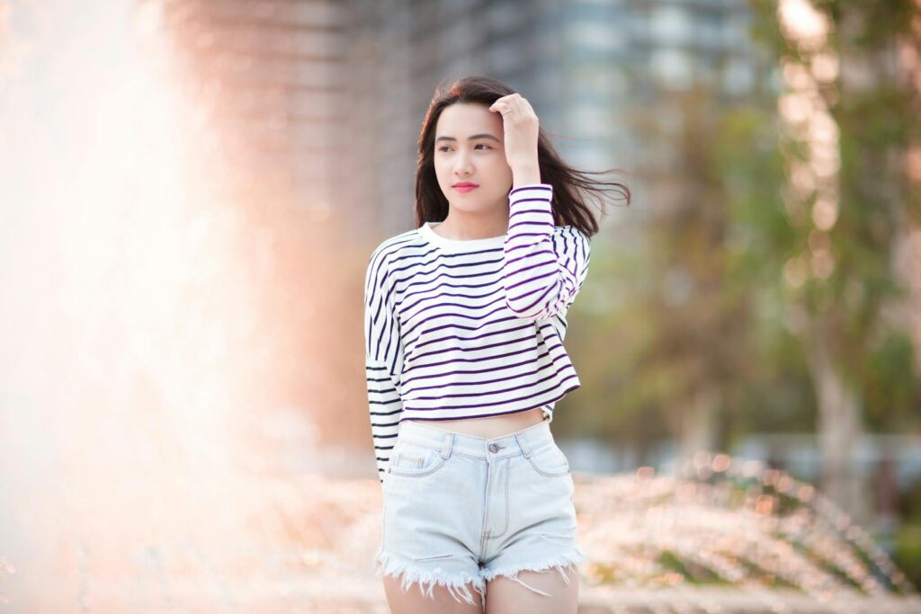 A teenage girl in a striped top and denim shorts enjoying a sunny day outdoors.