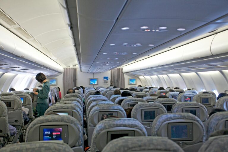 Interior view of a commercial airplane filled with passengers and cabin crew attending to travelers.