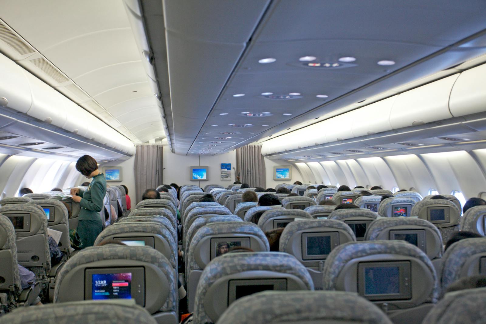 Interior view of a commercial airplane filled with passengers and cabin crew attending to travelers.
