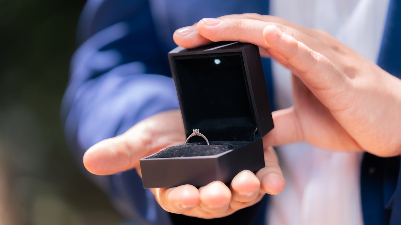 Close-up of a man holding a diamond engagement ring in a black box, symbolizing proposal.